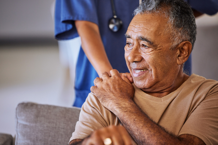 Nurse with comforting hand on shoulder of senior man